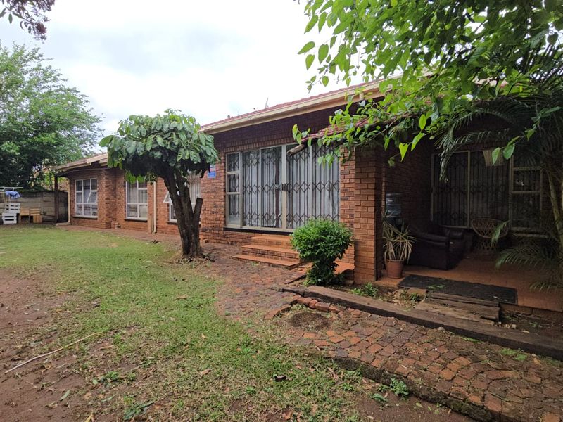 Rear view of a brick house featuring a covered patio, security gates, and a spacious garden area with a paved walkway.