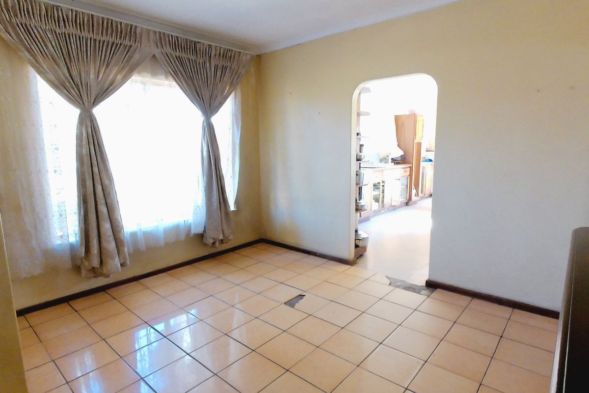 An empty living room featuring ceramic floor tiles and an arched doorway leading to the kitchen area.