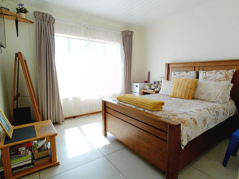 A bright bedroom featuring tiled flooring and a timber-look ceiling, offering a functional space with natural light from a large window.