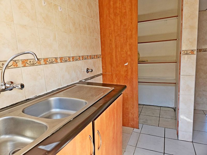A functional scullery area featuring a double stainless steel sink, tiled backsplash, built-in cabinetry, and open shelving for additional storage.