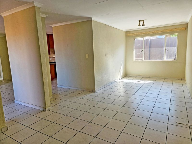 An empty open-plan living area featuring ceramic floor tiles, coved cornices, and a view into the adjacent kitchen space.