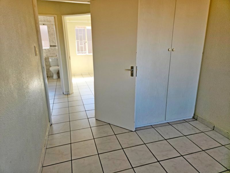 An empty bedroom featuring tiled flooring and built-in cupboards, with a view through to an adjacent bathroom and another room.