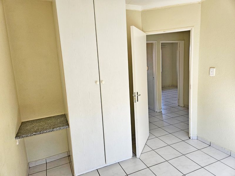 A vacant bedroom featuring tiled flooring, a built-in wardrobe, and a stone-topped vanity shelf, leading into a hallway.