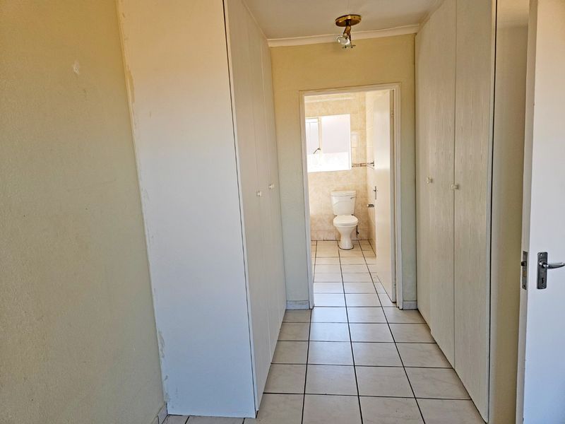 A hallway featuring extensive built-in cupboard storage, tiled flooring, and direct access to an adjacent bathroom.
