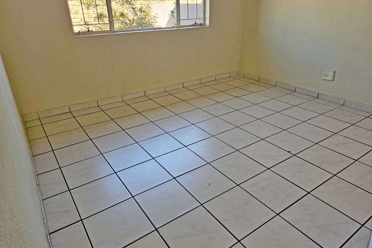 An empty bedroom featuring tiled flooring, a window with security bars, and neutral wall finishes, offering a blank canvas for potential interior design updates.