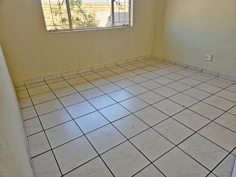 An empty bedroom featuring tiled flooring, a window with security bars, and neutral wall finishes, offering a blank canvas for potential interior design updates.