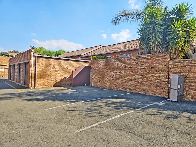 Exterior view of the townhouse complex featuring a paved parking area, brick boundary walls, and access to private garages.