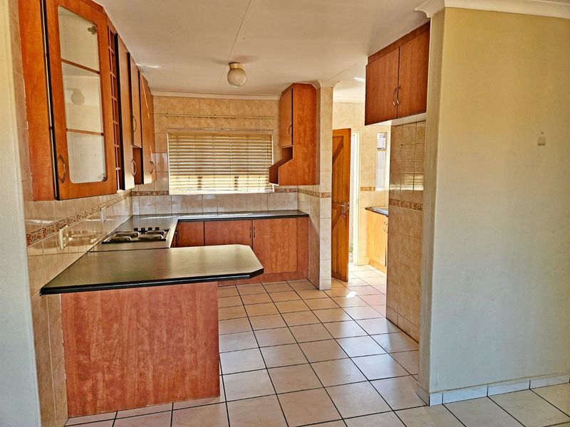A functional kitchen featuring laminate cabinetry, tiled flooring, and a built-in gas hob, offering a practical layout with potential for modern updates.