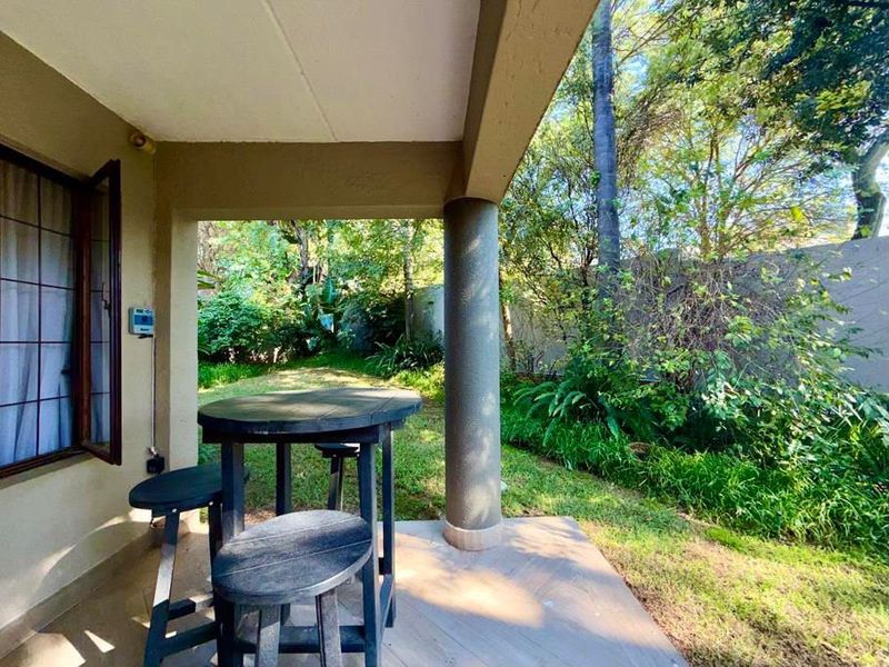 A covered patio area featuring tiled flooring and a structural column, overlooking a lush, private garden space.