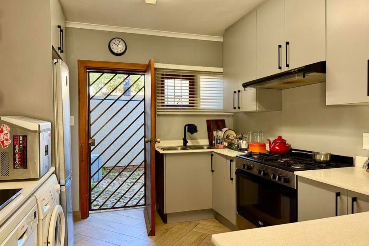 Functional kitchen featuring light grey cabinetry, gas stove with extractor, double sink, and direct access to an outdoor area through a security gate.