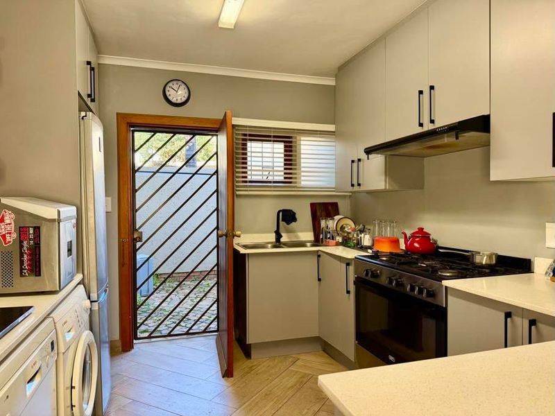 Functional kitchen featuring light grey cabinetry, gas stove with extractor, double sink, and direct access to an outdoor area through a security gate.