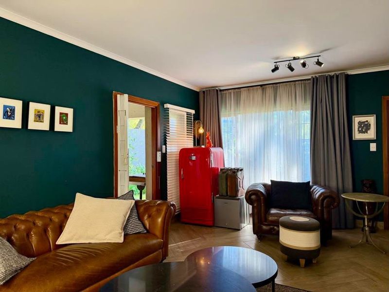 A cozy living room featuring dark green walls, herringbone flooring, and large windows with floor-to-ceiling curtains, providing a warm and inviting atmosphere.