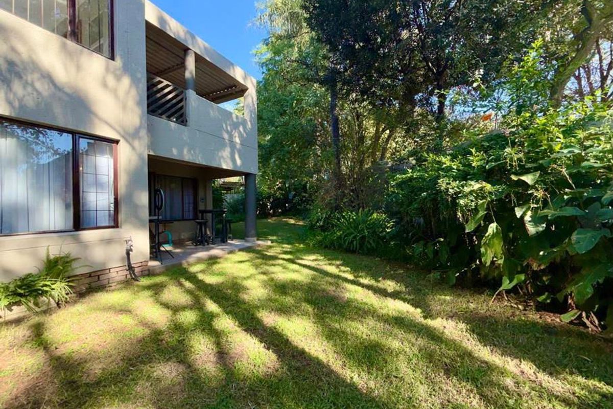 A rear view of the property featuring a covered patio area, a well-maintained lawn, and established garden trees.