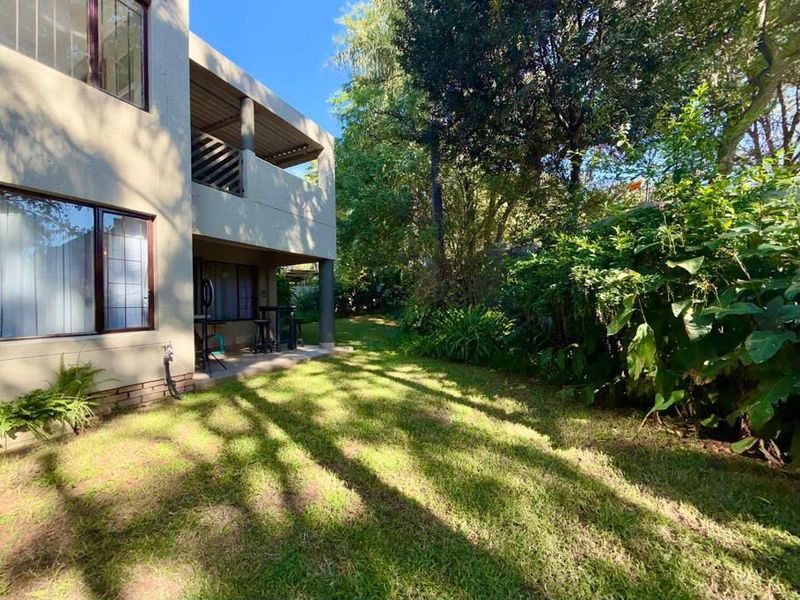 A rear view of the property featuring a covered patio area, a well-maintained lawn, and established garden trees.