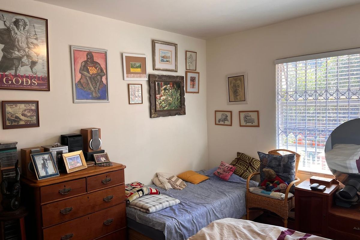 A cozy bedroom featuring neutral walls, natural light through a window with security bars, and space for a bed and storage furniture.