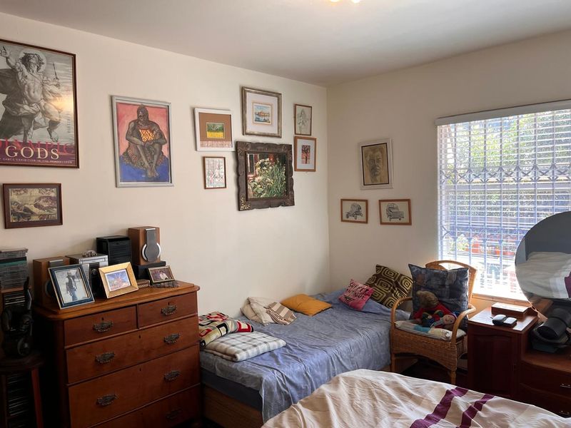 A cozy bedroom featuring neutral walls, natural light through a window with security bars, and space for a bed and storage furniture.
