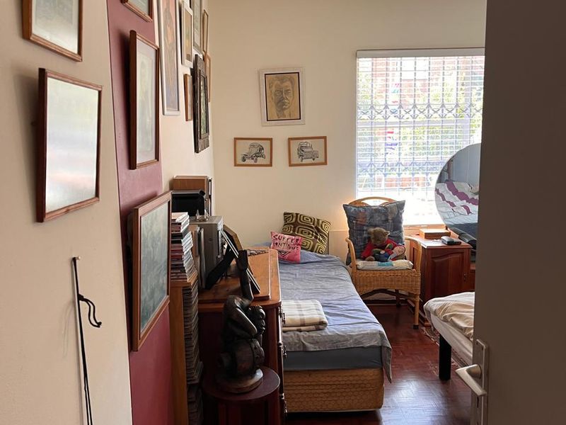 A bedroom featuring parquet flooring and a window fitted with security bars, offering a functional space with potential for modernization.