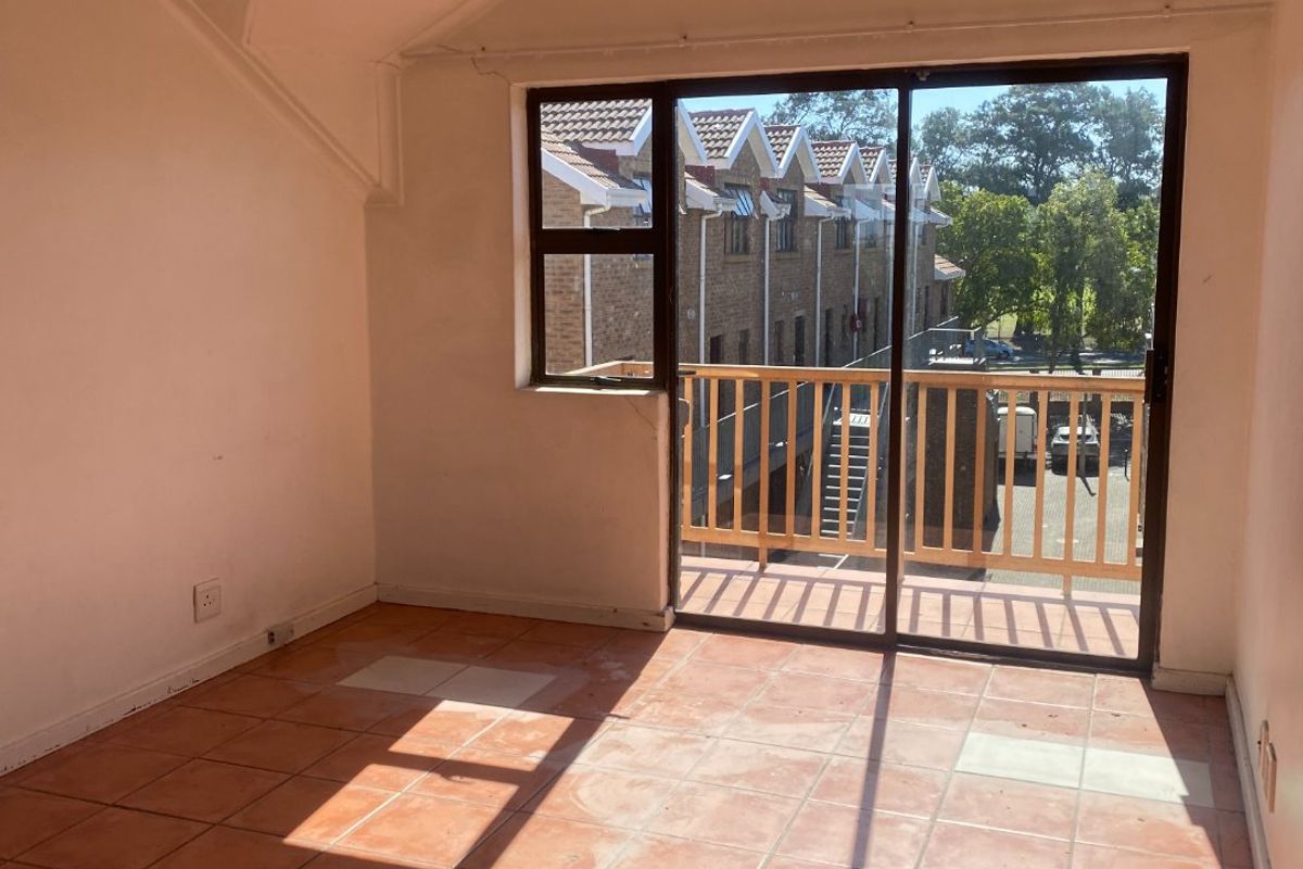 An empty bedroom featuring vaulted ceilings, terracotta-style tiled flooring, and a sliding glass door leading to a private balcony.