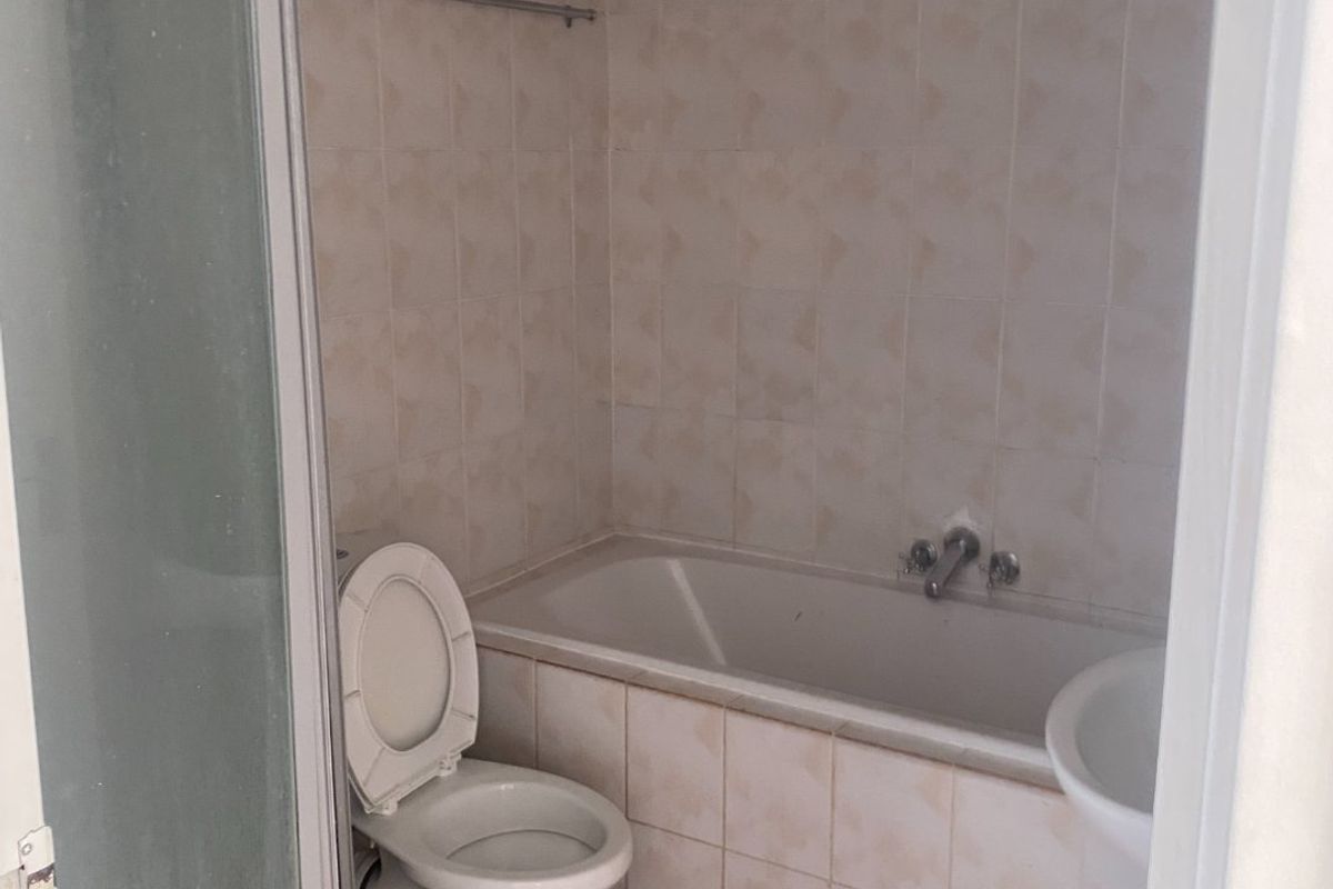 A dated bathroom featuring a bathtub, toilet, pedestal basin, and shower enclosure with tiled finishes, currently requiring maintenance and cosmetic updates.