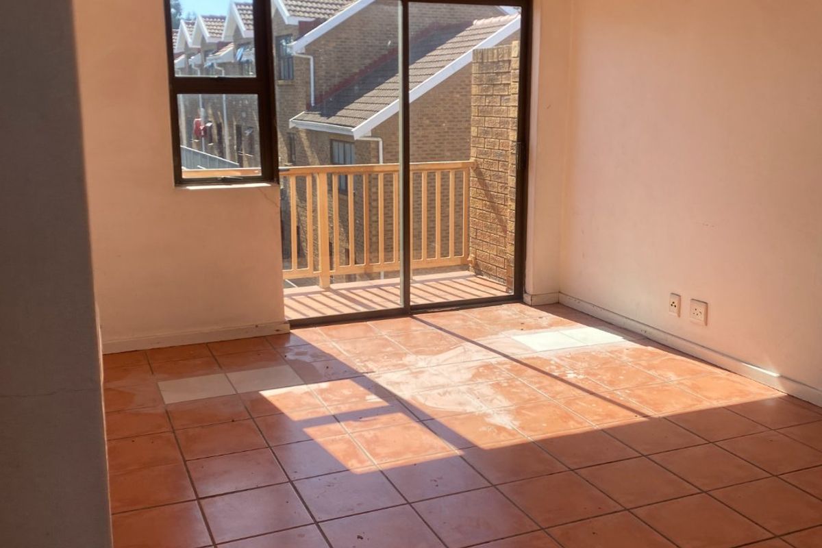 An empty living room featuring vaulted ceilings, ceramic tile flooring, and a sliding glass door providing access to a private balcony.
