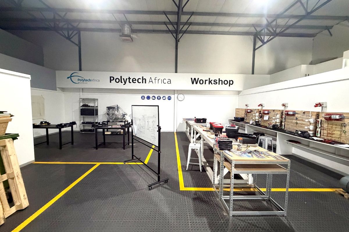 A well-maintained industrial workshop space featuring exposed steel roof trusses, durable rubberized flooring, and extensive wall-mounted pegboard storage systems.