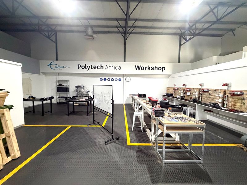 A well-maintained industrial workshop space featuring exposed steel roof trusses, durable rubberized flooring, and extensive wall-mounted pegboard storage systems.