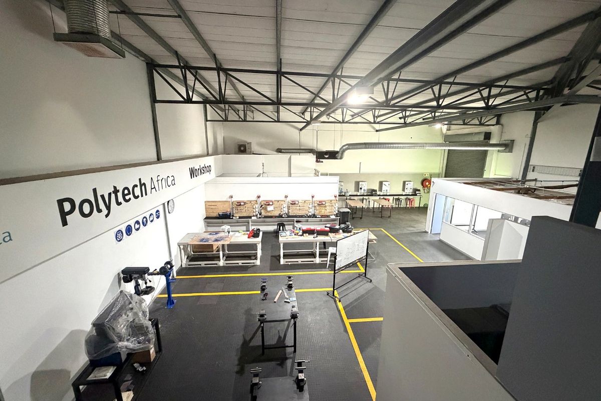 Spacious industrial workshop featuring high ceilings with exposed steel trusses, durable epoxy flooring, and integrated ventilation systems, suitable for various technical or manufacturing operations.