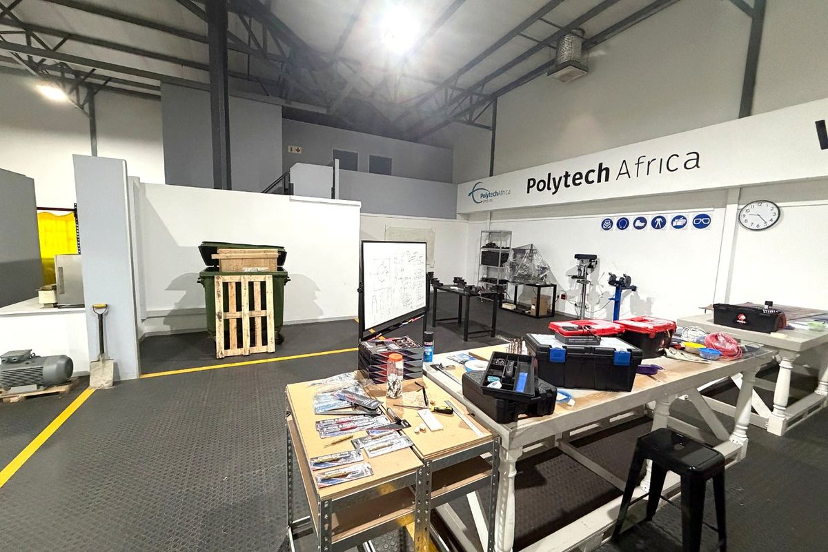 Spacious industrial utility area featuring exposed steel roof trusses, durable rubber flooring, and high-bay lighting, currently utilized as a workshop space.