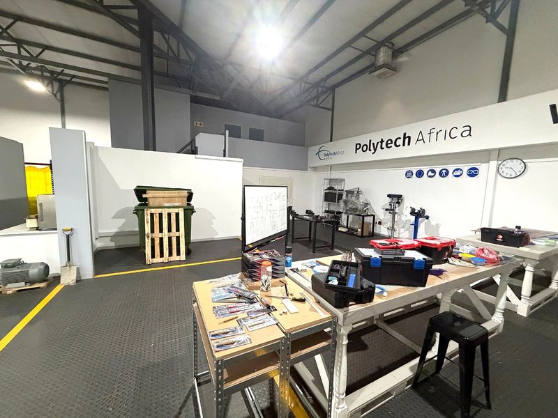 Spacious industrial utility area featuring exposed steel roof trusses, durable rubber flooring, and high-bay lighting, currently utilized as a workshop space.