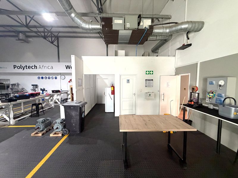 Industrial workshop space featuring exposed ventilation ductwork, durable rubber flooring, safety equipment, and functional partitioned utility areas.