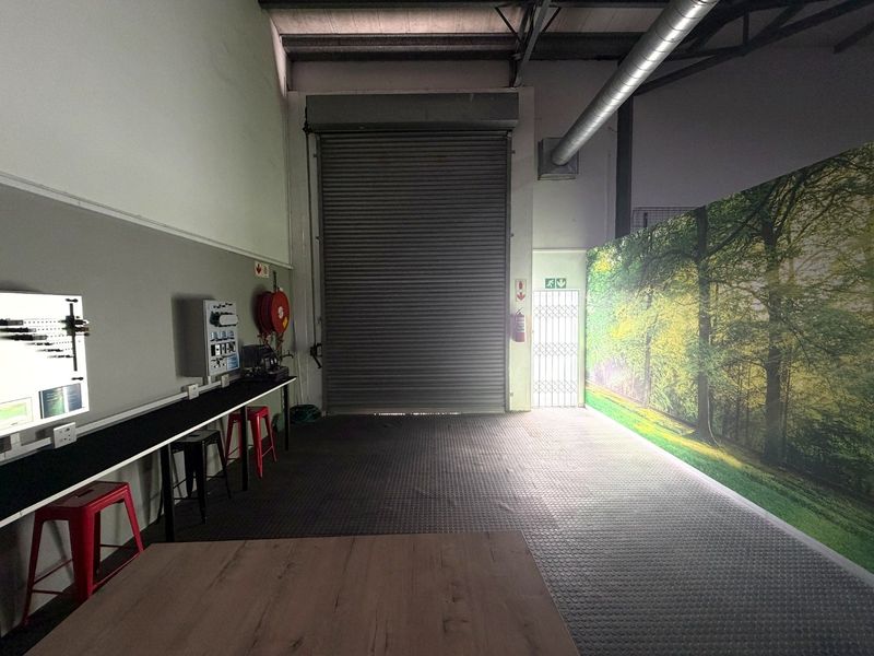Industrial utility space featuring a large roller shutter door, durable rubber flooring, exposed ceiling ducting, and integrated fire safety equipment.