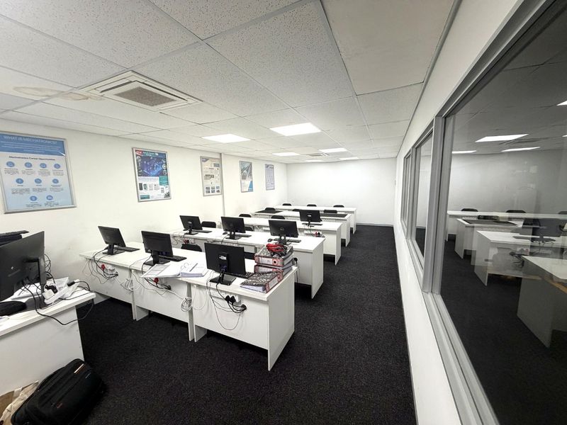 A functional office space featuring a suspended ceiling, recessed lighting, ducted air conditioning, and a glass partition wall overlooking an adjacent workspace.