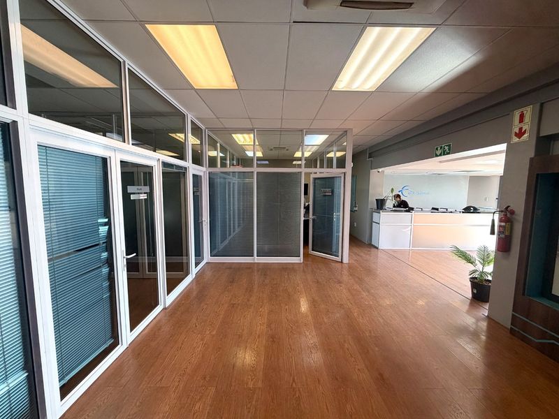 Modern industrial office space featuring laminate flooring, aluminum-framed glass partitions, and a dedicated reception area with integrated lighting.