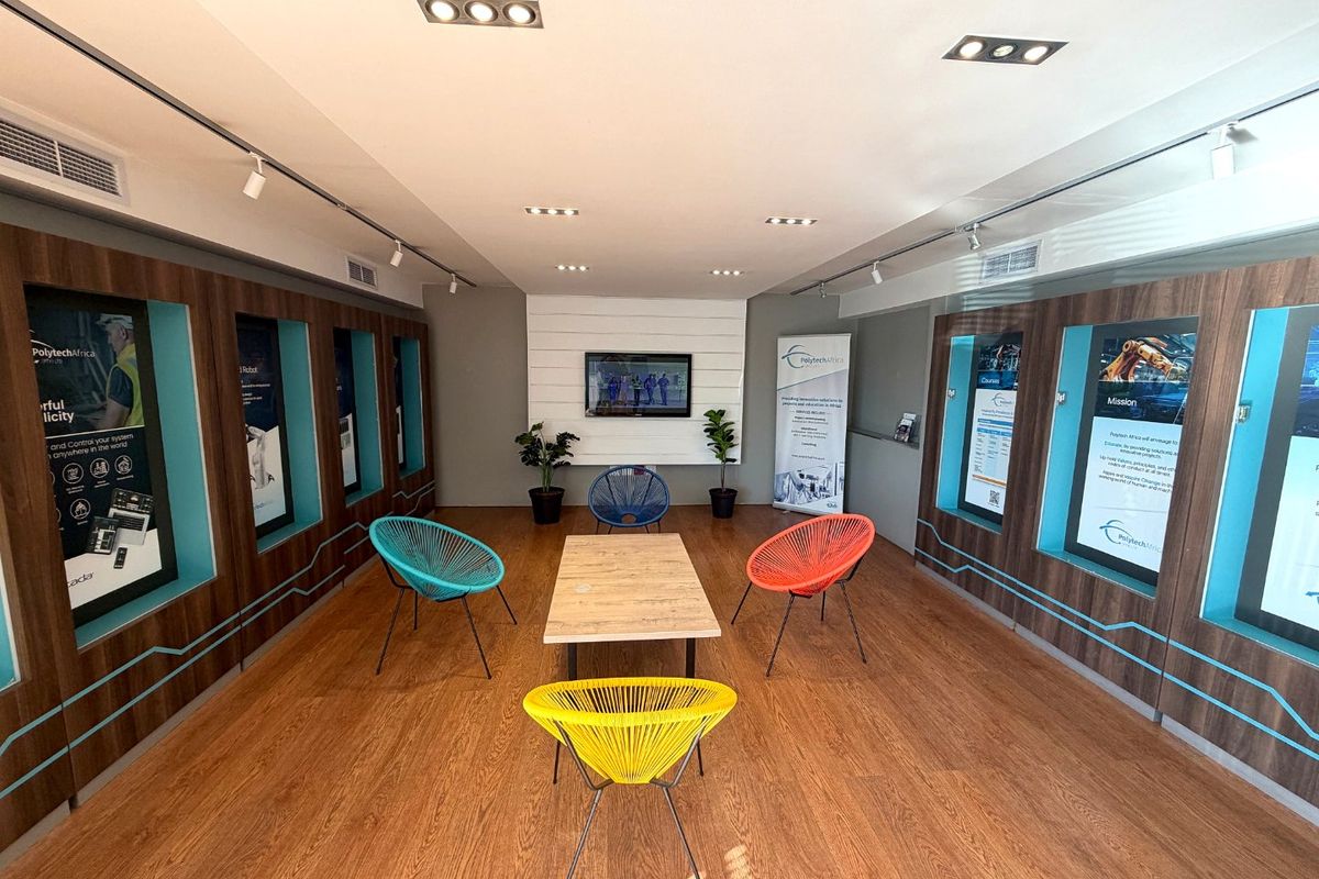 A modern, well-lit industrial office lounge area featuring wood-look laminate flooring, recessed ceiling lighting, and built-in display niches along the side walls.