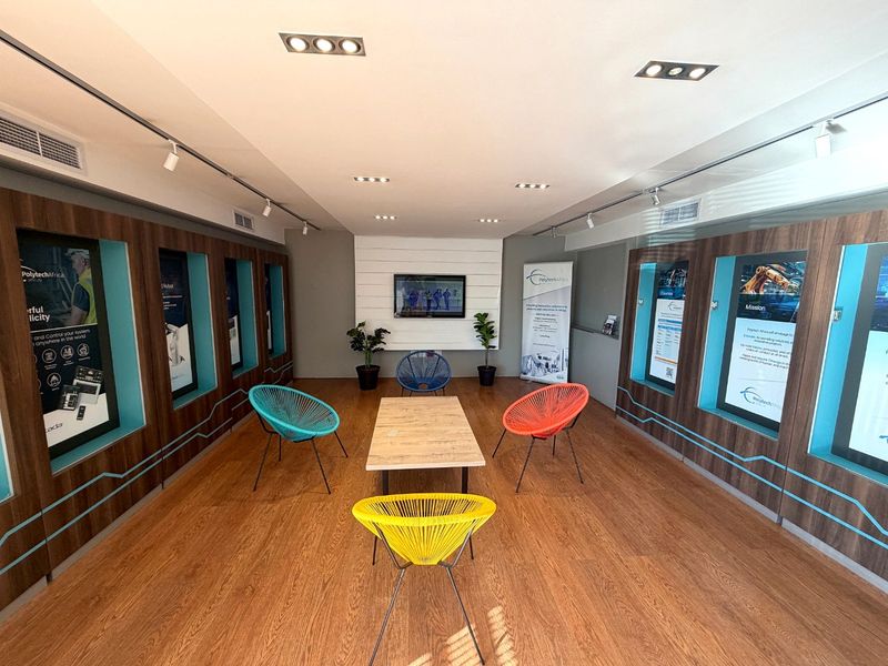 A modern, well-lit industrial office lounge area featuring wood-look laminate flooring, recessed ceiling lighting, and built-in display niches along the side walls.