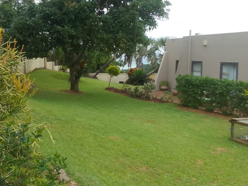 A spacious rear garden featuring a well-maintained lawn, mature trees, boundary walling, and a built-in outdoor braai area.