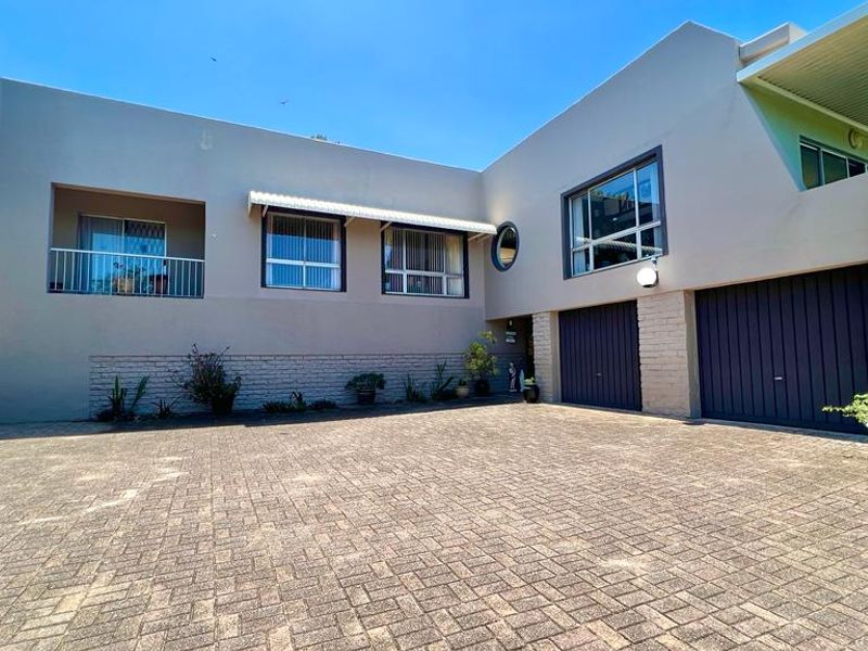 Front elevation of a multi-level house featuring a paved driveway, double garage, and an upper-level balcony with metal railings.