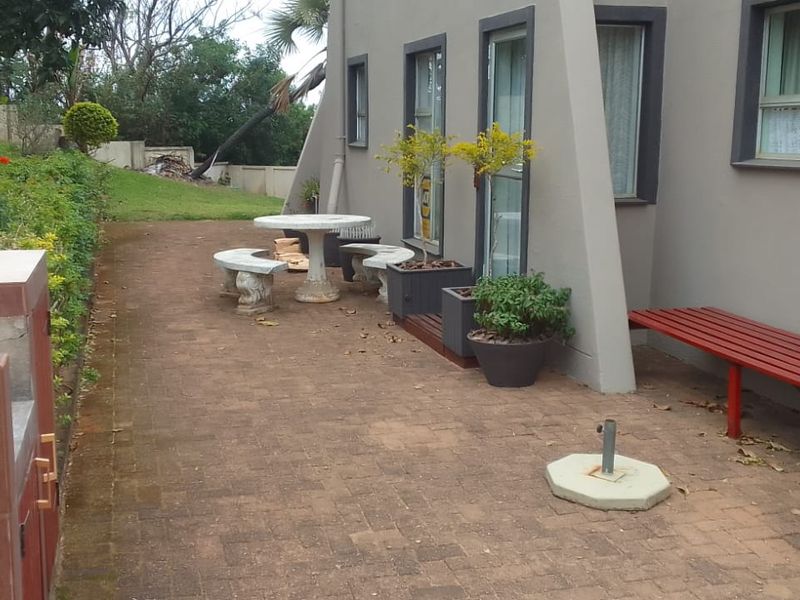 A paved rear patio area featuring a built-in braai, overlooking a garden space with a retaining wall.