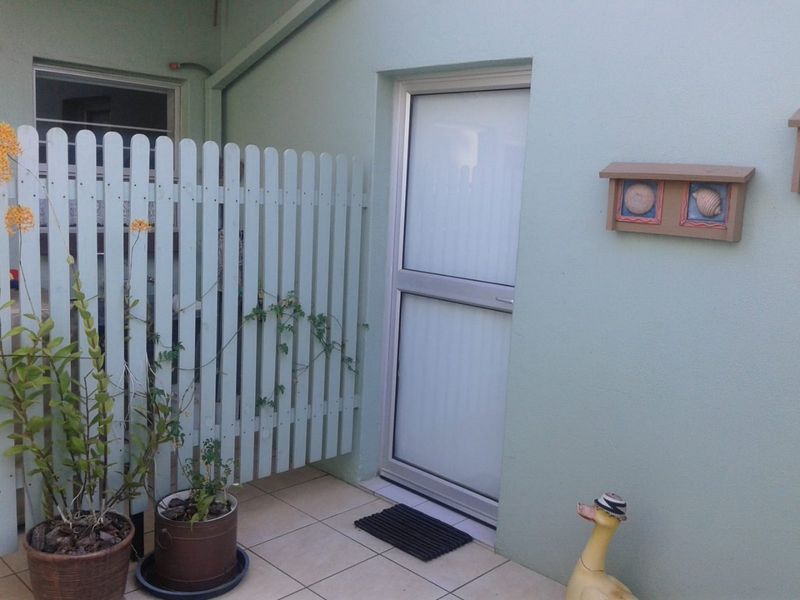 A small, tiled outdoor patio area featuring a privacy picket fence and an aluminium framed door providing access to the home.
