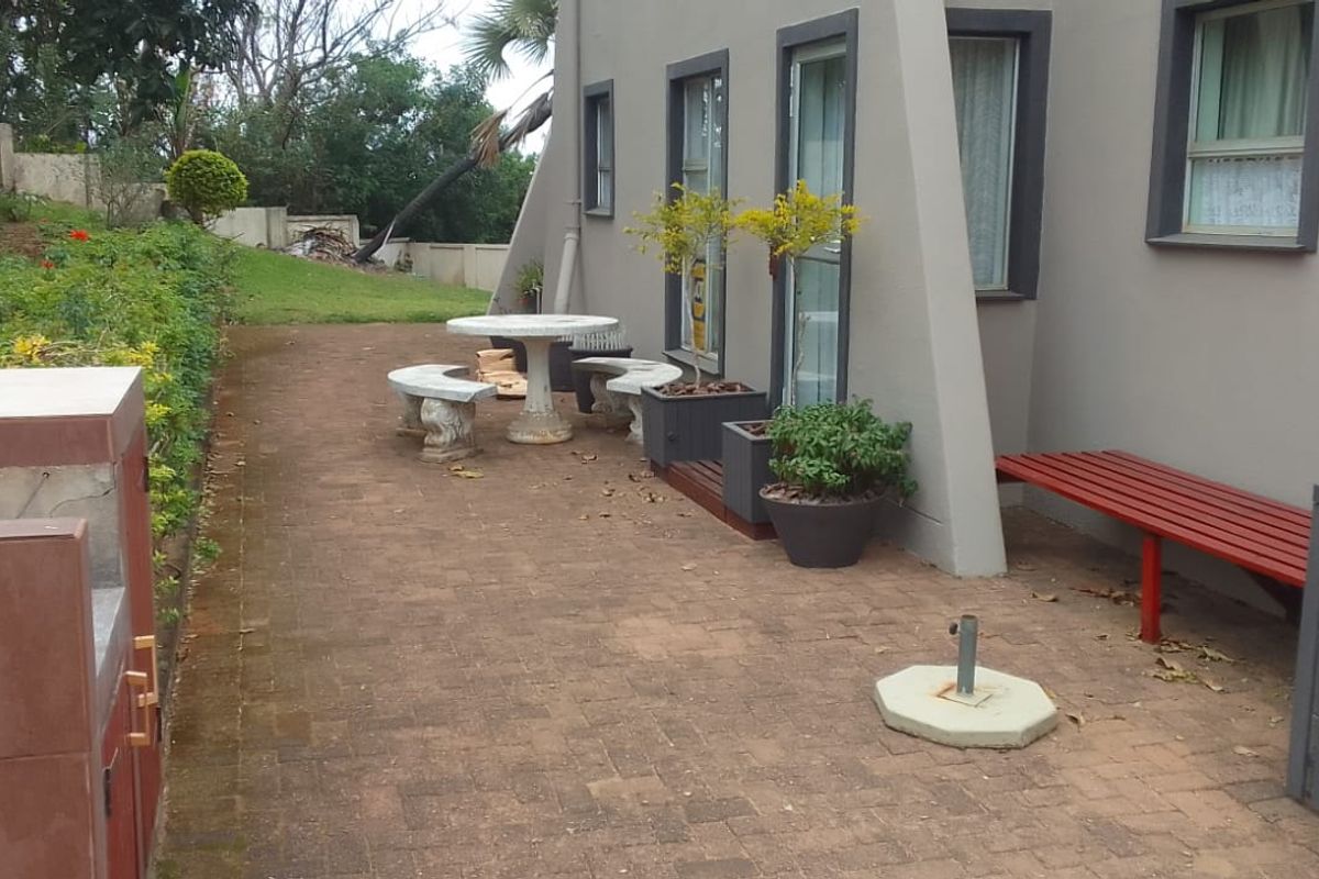 A paved rear patio area featuring a built-in braai, overlooking a garden space with a retaining wall.