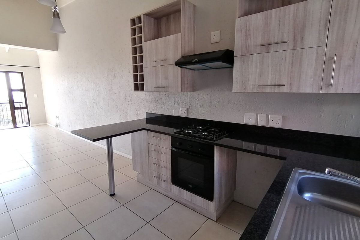 Modern kitchen featuring light wood-grain cabinetry, granite countertops, built-in gas hob, oven, and extractor fan, with an integrated breakfast bar and tiled flooring.