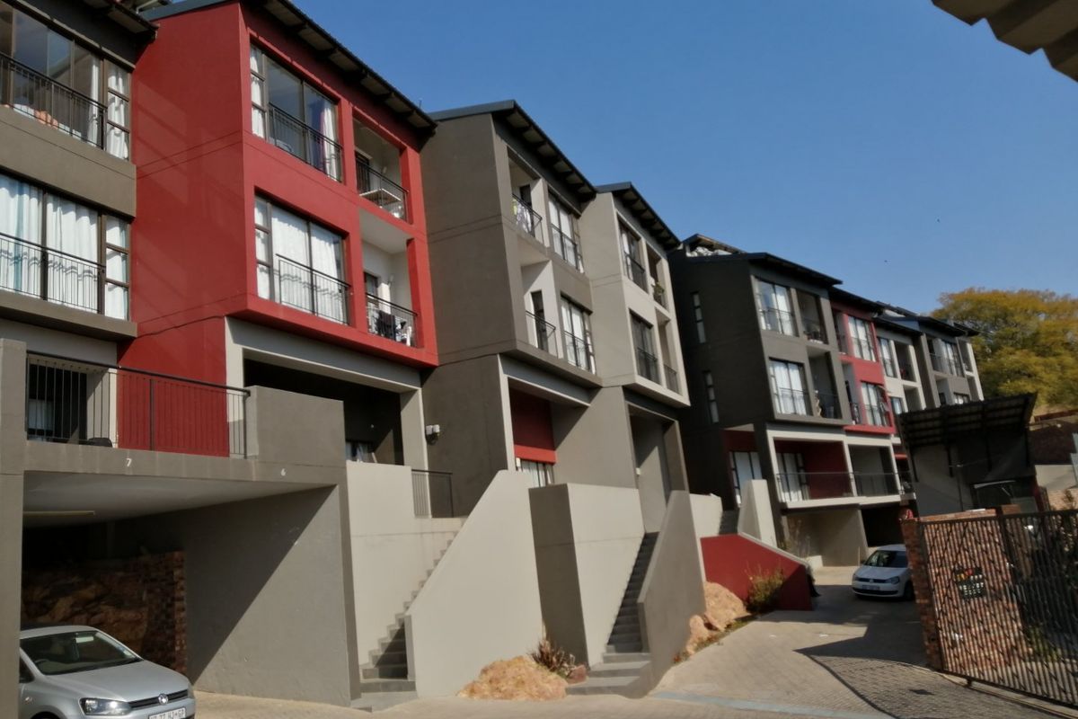 Modern multi-story apartment complex featuring red and grey facade accents, private balconies, and paved driveway access.