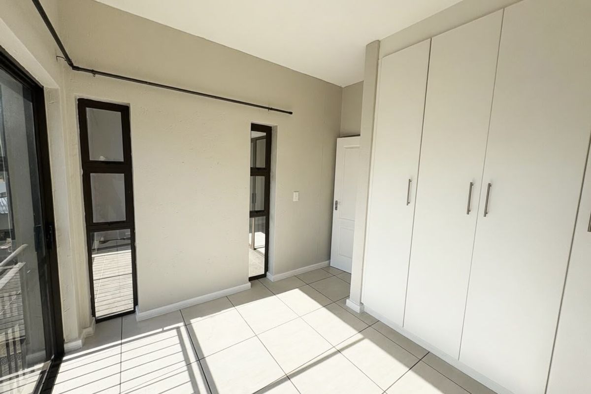 A bright, empty bedroom featuring neutral tiled flooring, built-in cupboards, and access to a balcony through a sliding door.