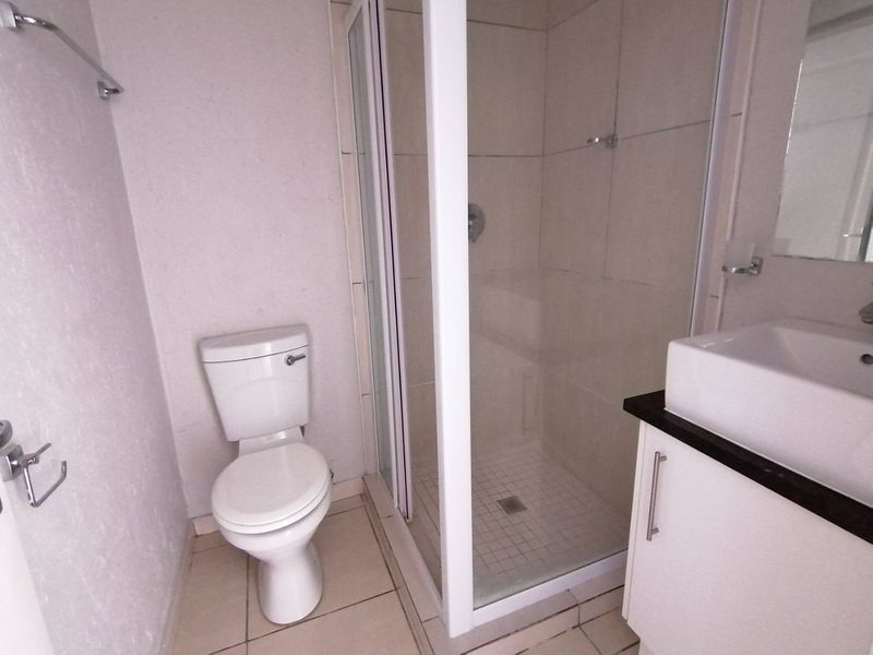 A functional bathroom featuring a shower enclosure, a white toilet, and a vanity cabinet with a basin.