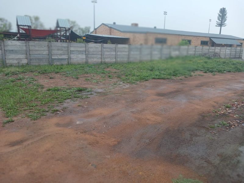 A view of a vacant residential plot featuring an unpaved surface and a precast concrete boundary wall.