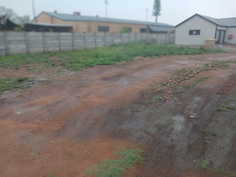An unpaved rear yard area featuring a precast concrete boundary wall and an adjacent outbuilding structure.