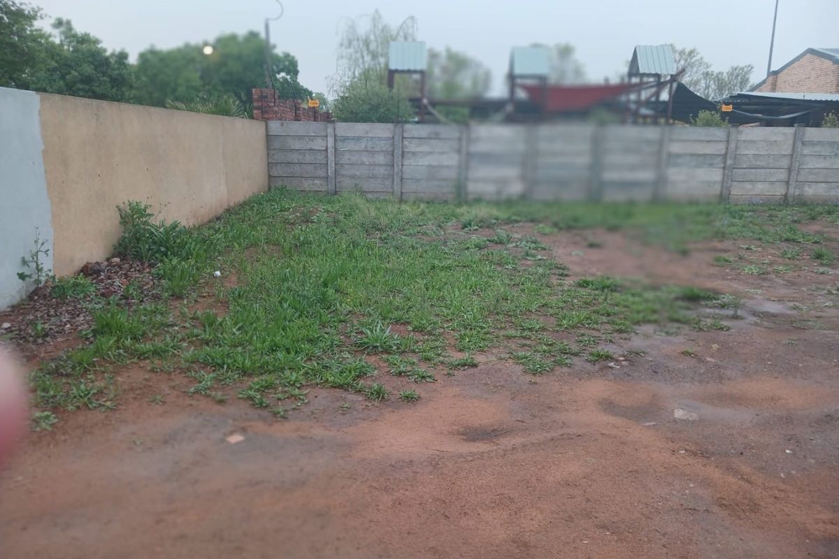 A view of the rear vacant land area featuring precast concrete and plastered boundary walls with natural ground cover.