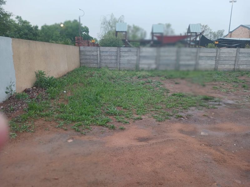 A view of the rear vacant land area featuring precast concrete and plastered boundary walls with natural ground cover.