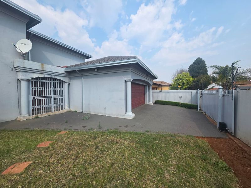 Front exterior view of the property featuring a paved driveway, garage, and secure gated entrance with boundary walling.