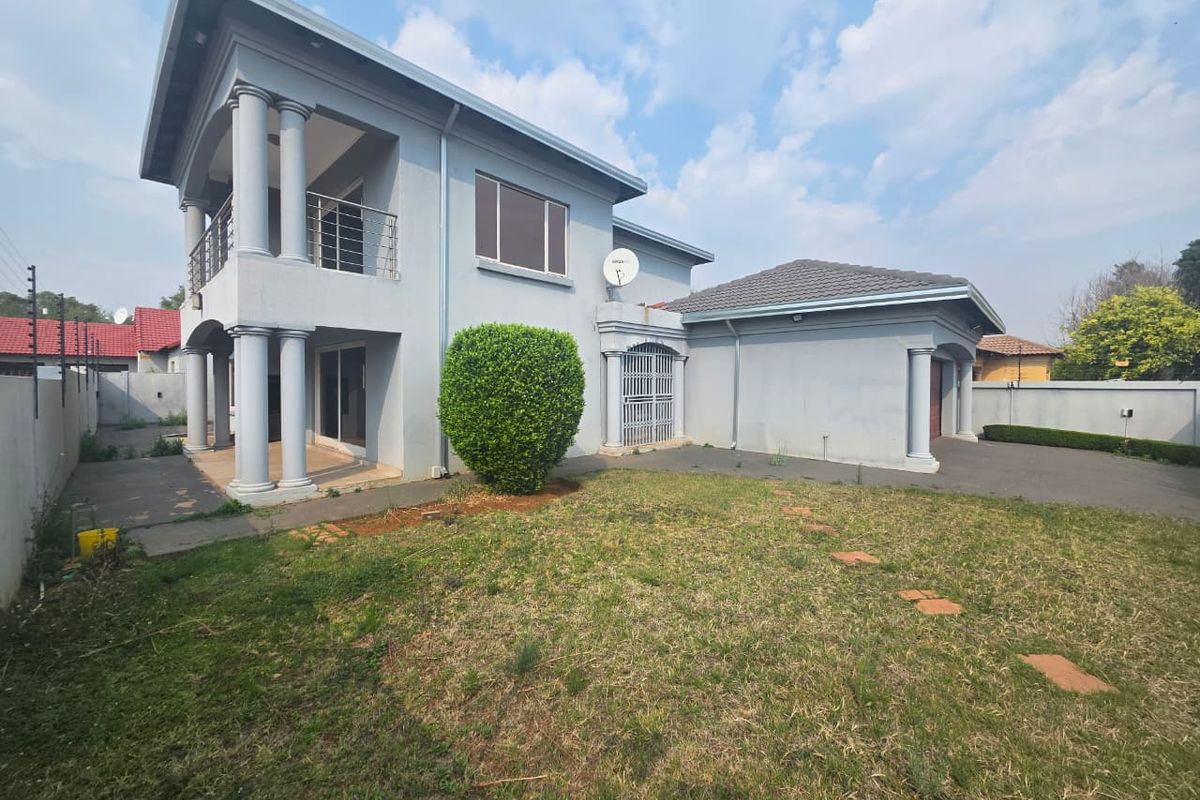 Rear view of a double-storey house featuring a balcony with metal railings, concrete columns, paved driveway, and a private garden area.